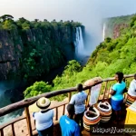 잠비아 관광 수익 - Photorealistic wide-angle scene of Victoria Falls in Zambia at golden sunrise, mist glowing above th...
